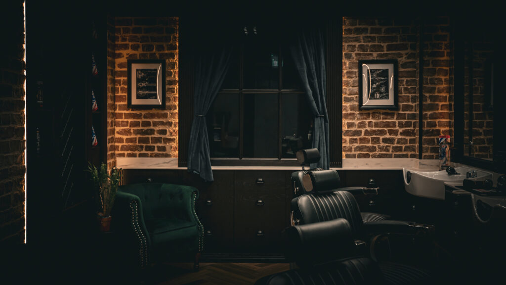 Dimly lit studio corner with a barber chair, exposed brick, and dark curtains.