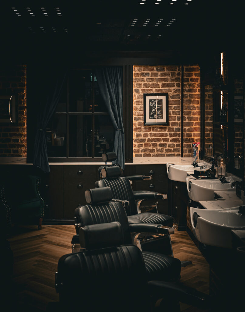 Low-lit interior with barber chairs and wash basins against exposed brick.